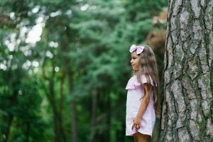 Beautiful girl in a pink dress stands near a tree in the forest and dreams photo