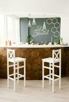A stylish modern bar counter decorated with wooden tiles and two white bar stools in the living room of the house. Scandinavian interior design photo