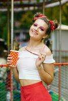 un bonito niña sostiene un papel eco vaso en su manos y camina en el verano al aire libre en un diversión parque foto