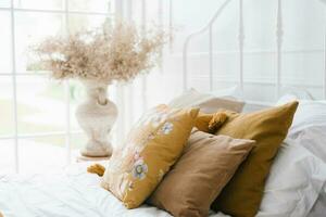 Mustard-colored pillows on a white bed standing by the window in a modern bedroom photo