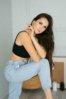 Sensual beautiful young Caucasian woman hugs herself by the shoulders in a black top and jeans photo