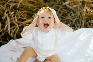 An emotional child a boy in white clothes is relaxing in the fresh air in a field and holding his hands on his head wondering photo