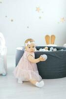 Little girl holds balls in her hands and plays with them, sitting near the pool with colorful balls photo