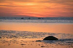 Sunset, small rock at low tide in front of the illuminated sea. Light waves photo