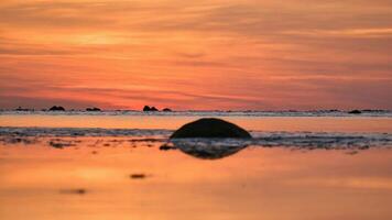 Sunset, small rock at low tide in front of the illuminated sea. Light waves photo