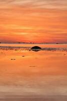 Sunset, small rock at low tide in front of the illuminated sea. Light waves photo