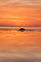 atardecer, pequeño rock a bajo marea en frente de el iluminado mar. ligero olas foto