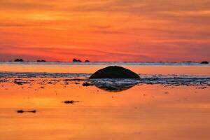 Sunset, small rock at low tide in front of the illuminated sea. Light waves photo
