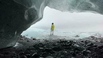 turista mulher ficar de pé de lindo fjallsjkull geleira dentro Islândia dentro nublado dia. gelo cavernas dentro Islândia. Visão a partir de pequeno Gap = Vão caverna video