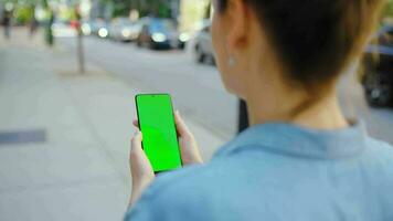 mujer es yendo a lo largo el calle y utilizando teléfono inteligente con verde pantalla video