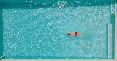 parte superior abajo ver de un hombre en rojo pantalones cortos nadando en el piscina, lento movimiento. video