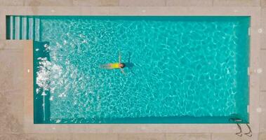 top naar beneden visie van een vrouw in geel zwempak aan het liegen Aan haar terug in de zwembad. video