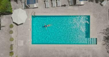 parte superior abajo ver de un mujer en azul traje de baño acostado en su espalda en el piscina. video