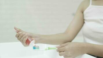 femelle mains écraser dentifrice de une tube sur une brosse à dents dans le salle de bains. video