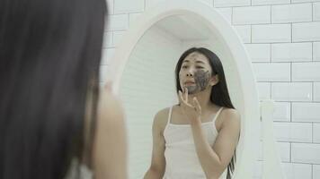 joven mujer aplicando cara máscara en baño y sonriente. hermosa hembra en frente de espejo. video