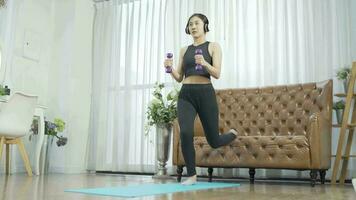 mujer perdiendo peso a hogar y hacer ejercicio con mancuernas vistiendo auriculares escuchando durante ejercicio. video