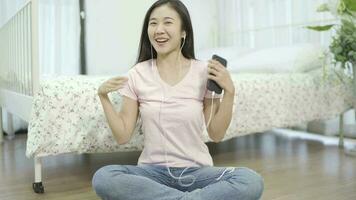 Young woman in casual clothes listening to music in headphones and singing while sitting on the floor near. video