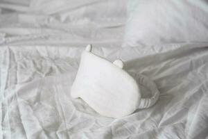 Sleep eye mask lying on white bedding. Awaking or insomnia concept. photo