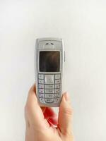 A hand holding old mobile phone on white background, early wireless digital technology, communication device photo