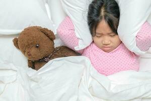 Little girl trying to sleep covering ears to avoid neighbor noise at home or hotel, photo