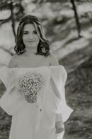 Awesome bride in a long wedding dress with a beautiful bouquet in hand and with charming smile. Under the tree in the beautiful sunset light in the park. photo