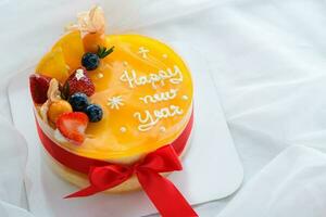 Orange cake with happy new year and topped with orange, strawberry, blueberry and Cape Gooseberry photo