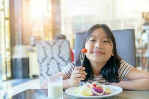Asian cute little girl eating fresh tomato and salad on morning. photo