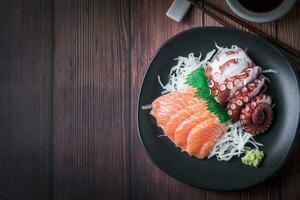 salmón y tako sashimi en negro plato con palillos foto