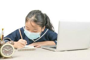 Asian student wearing protective mask,taking notes from laptop computer isolated on white photo