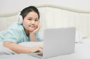 Obese schoolboy lying and wearing headphones to learn online from a laptop photo