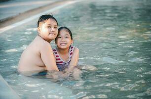 Happy brother and sisiter are playing water at swimming pool, photo