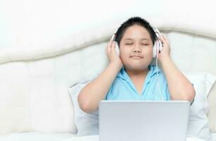 Cute happy Asian boy wearing headphones to listen music from laptop photo