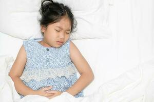 asian child suffering from stomachache and lying on bed. photo