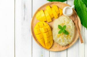 Ripe mango and sticky rice with coconut milk on white wood background photo