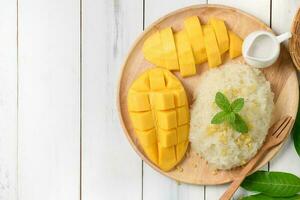 Ripe mango and sticky rice with coconut milk on white wood background photo