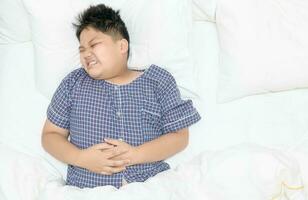 Obese fat boy suffering from stomachache and lying on bed. photo