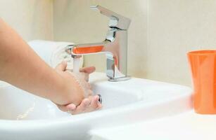 Washing hands child rinsing soap with running water at sink, photo