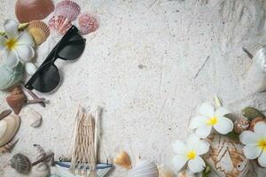 Sunglasses with Shells and plumeria flowers on sand background, photo