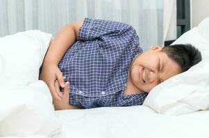 asian child suffering from stomachache and lying on bed. photo