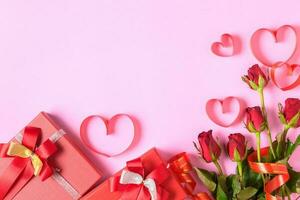 Red roses and gift box with heart red ribbon on pink background, photo