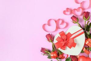 Red roses and gift box with heart red ribbon on pink background, photo