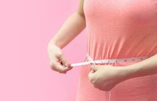 Cute young woman measuring her waist isolated on pink photo