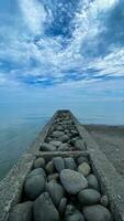 Pile of stones on the beach with blue sky and clouds in the background photo