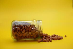 open glass jar filled to the brim with shelled nuts. glass bottle filled with peanuts isolated on yellow background. photo