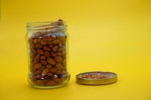 open glass jar filled to the brim with shelled nuts. glass bottle filled with peanuts isolated on yellow background. photo