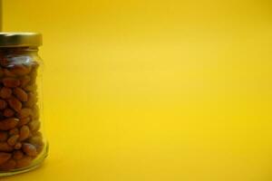 glass jar filled to the brim with shelled nuts. glass bottle filled with peanuts isolated on yellow background. photo