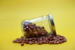 a glass jar half filled with shelled peanuts on top of a pile of peanuts. photo