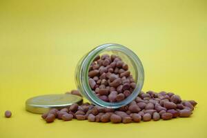 a glass jar half filled with shelled peanuts on top of a pile of peanuts. photo