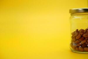 Half filled closed glass jar with peeled nuts isolated on yellow background. photo