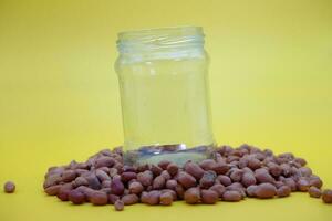 empty glass jar on a pile of peeled nuts isolated on yellow background photo